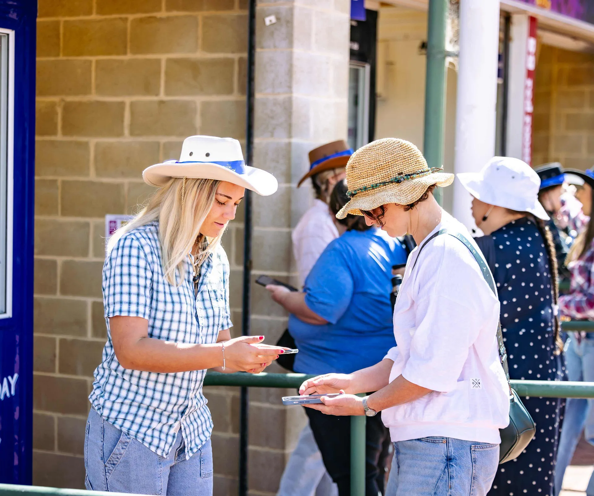 Two women in hats scanning tickets on their phones at Claremont Showground entrance