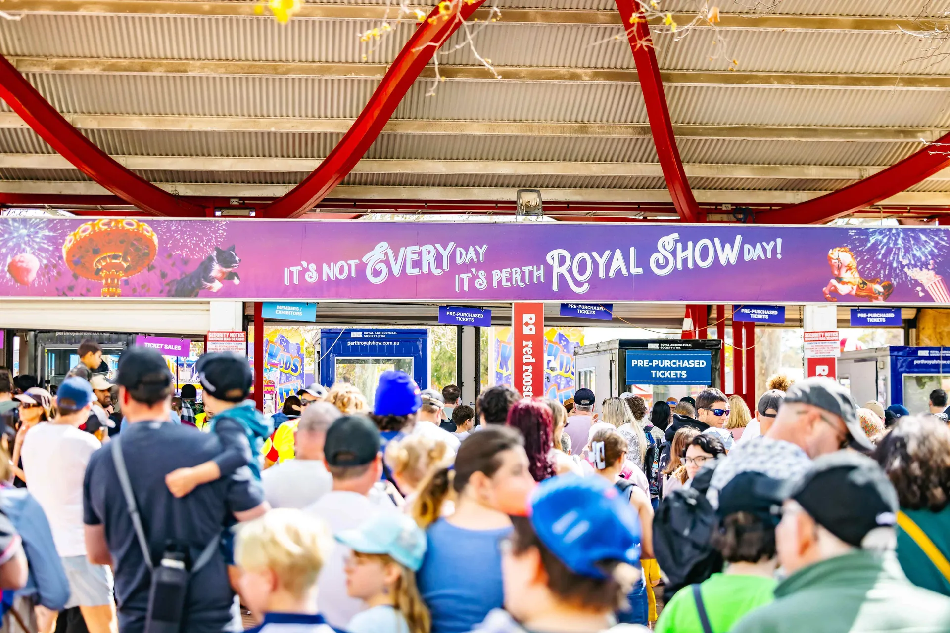 Crowds entering the Perth Royal Show through the main gates beneath a colourful welcome banner.
