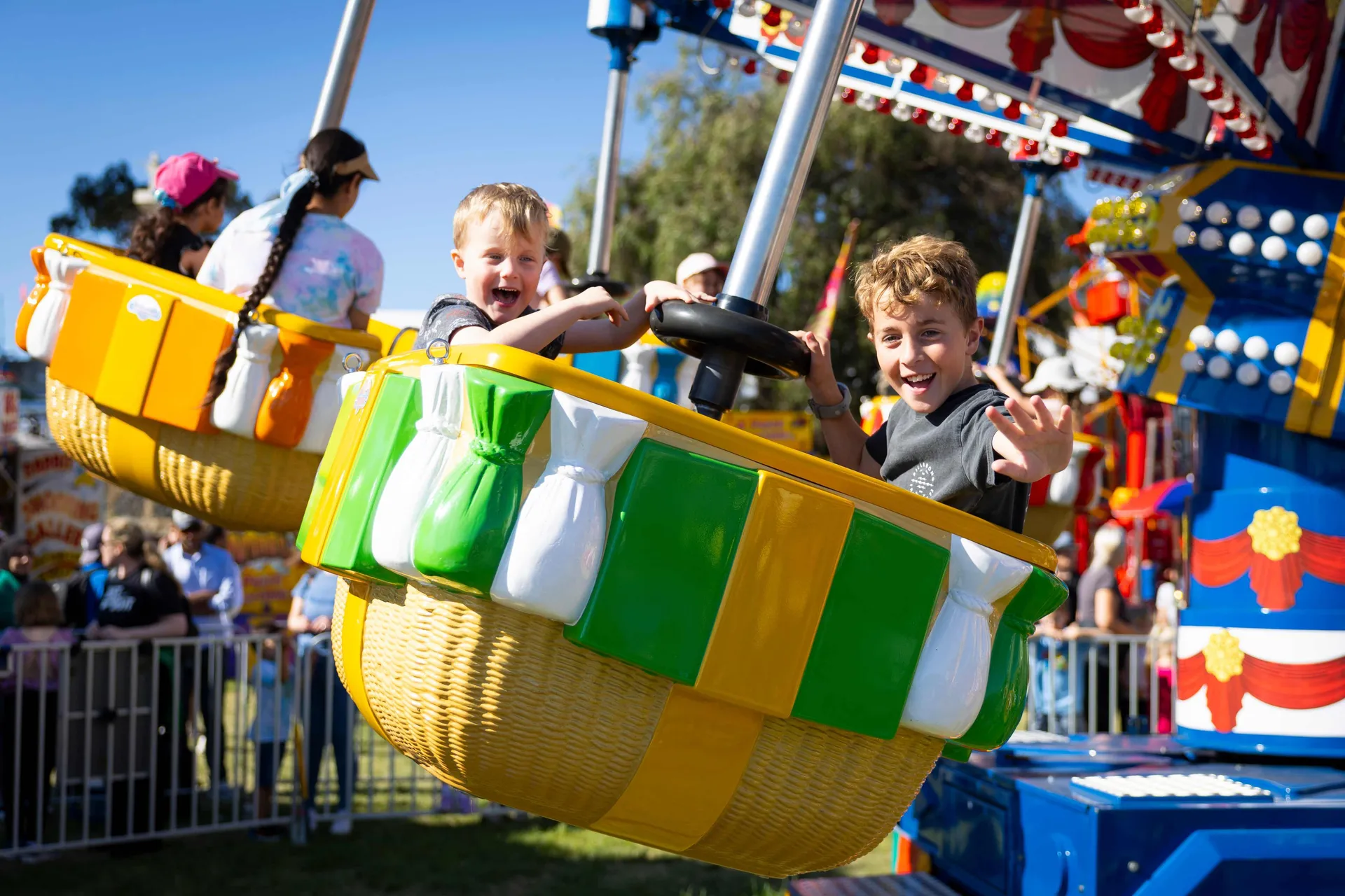 Children laughing and waving while riding a colourful spinning ride at the Perth Royal Show amusement area.