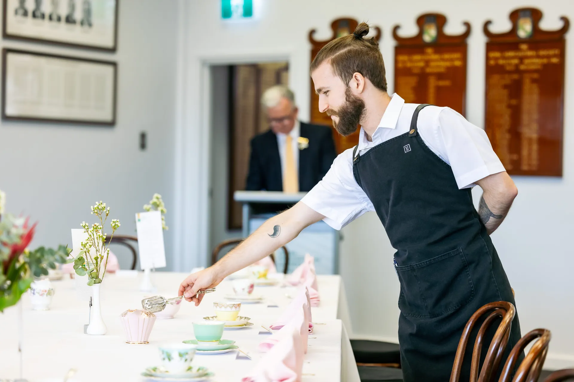 Caterer preparing a table setting for a formal event inside a function space at Claremont Showground.