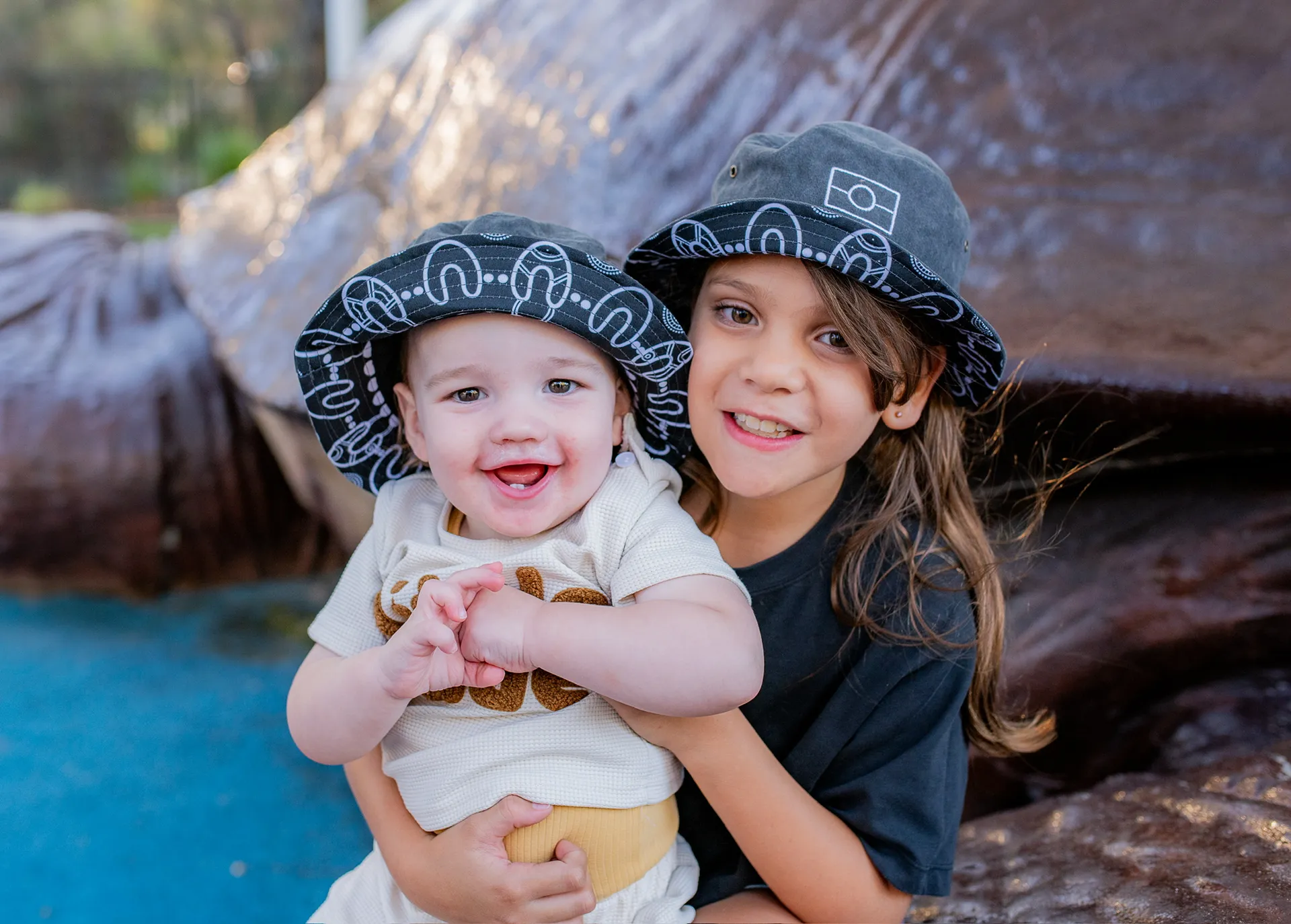 Baby and little girl both wearing Aboriginal artists patterned bucket hats