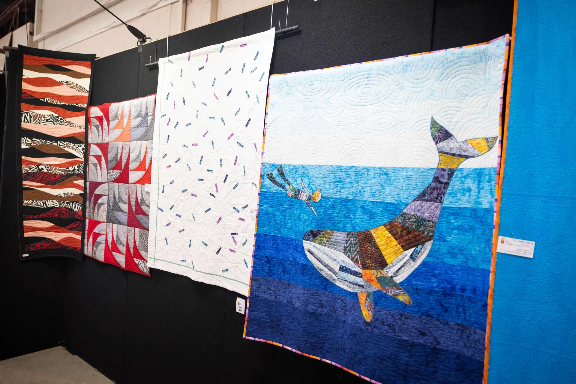 Colourful quilts displayed in the Creative Arts exhibition at the Perth Royal Show, including a large patchwork whale design in blue ocean tones alongside abstract patterned quilts.