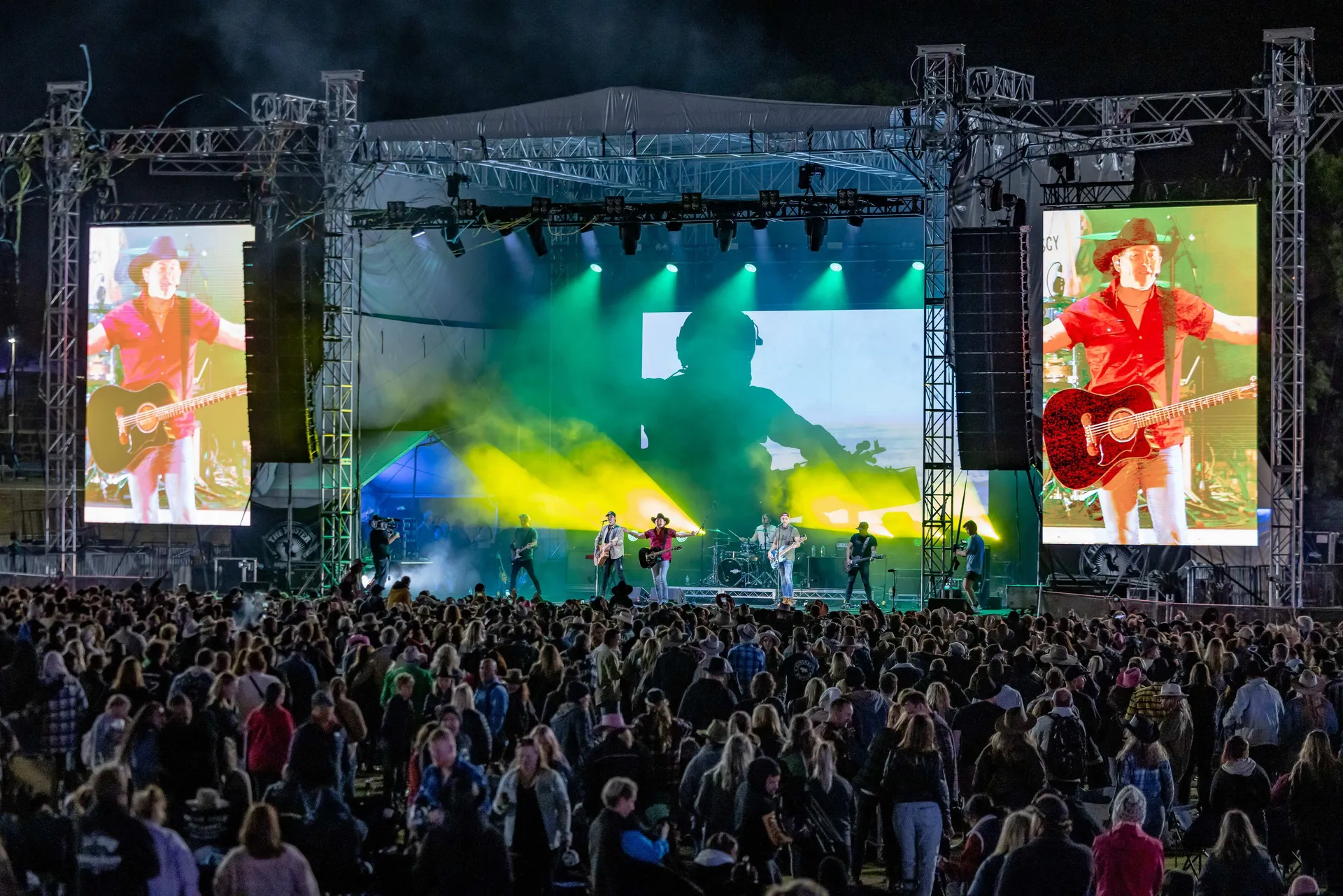 Large crowd watching a live country music performance on an outdoor stage at night