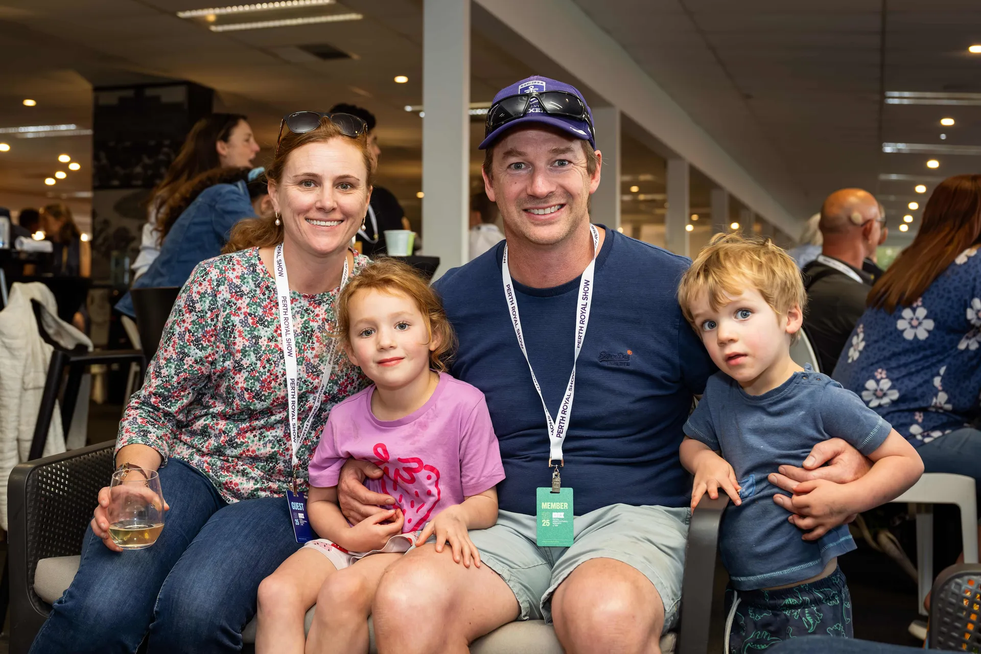 Family of four smiling at an indoor Perth Royal Show event, wearing Memebers lanyards.