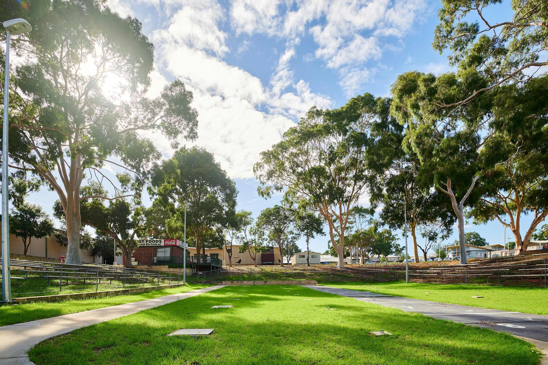Grassy open space surrounded by tiered seating and tall trees under a bright sky at Claremont Showground.
