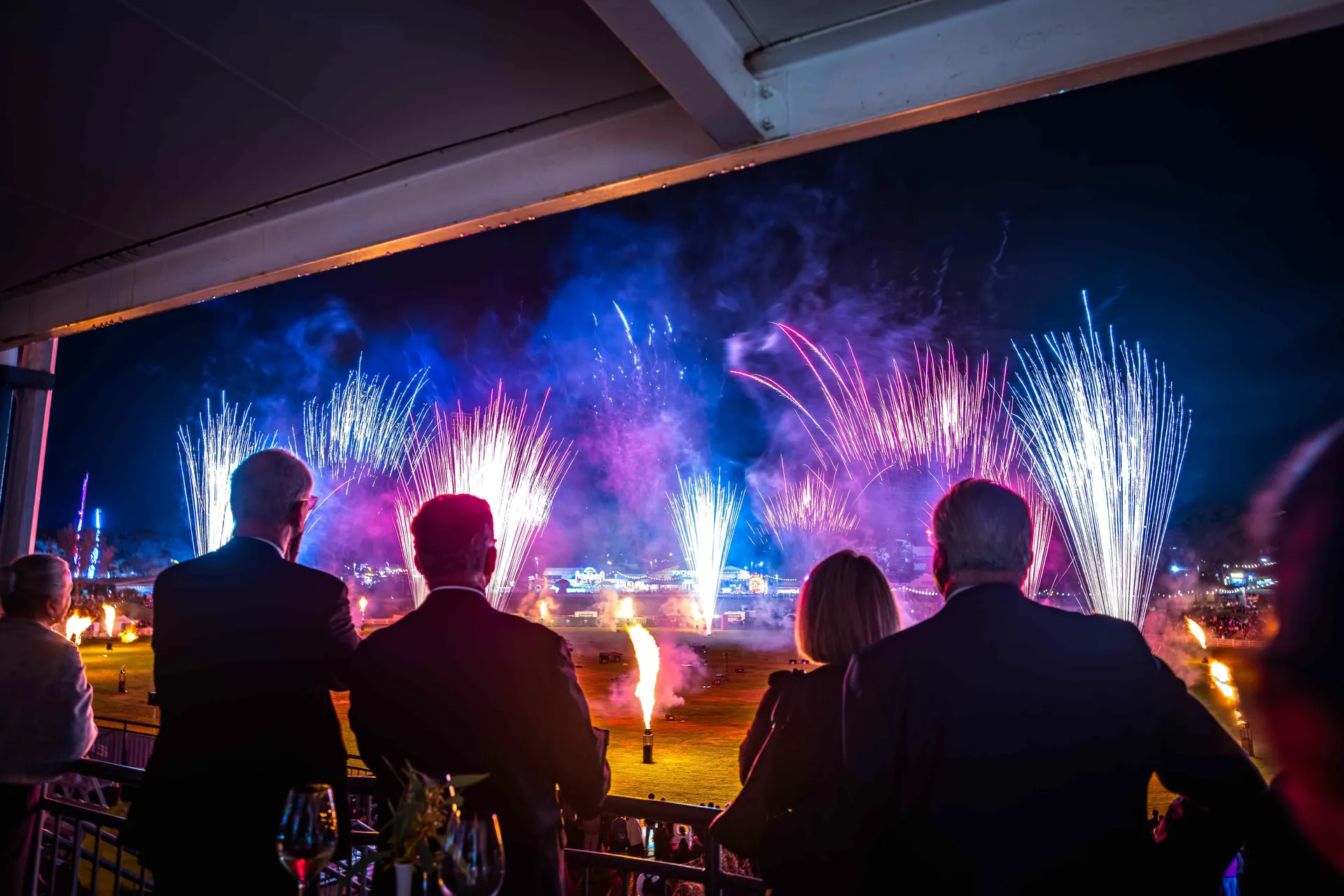People watching a colourful fireworks display over the Perth Royal Show grounds at night, viewed from a balcony.