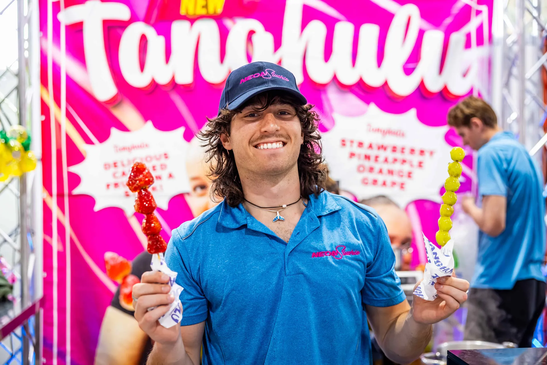 Vendor smiling while holding colourful candied fruit skewers at a food stall at the Perth Royal Show.