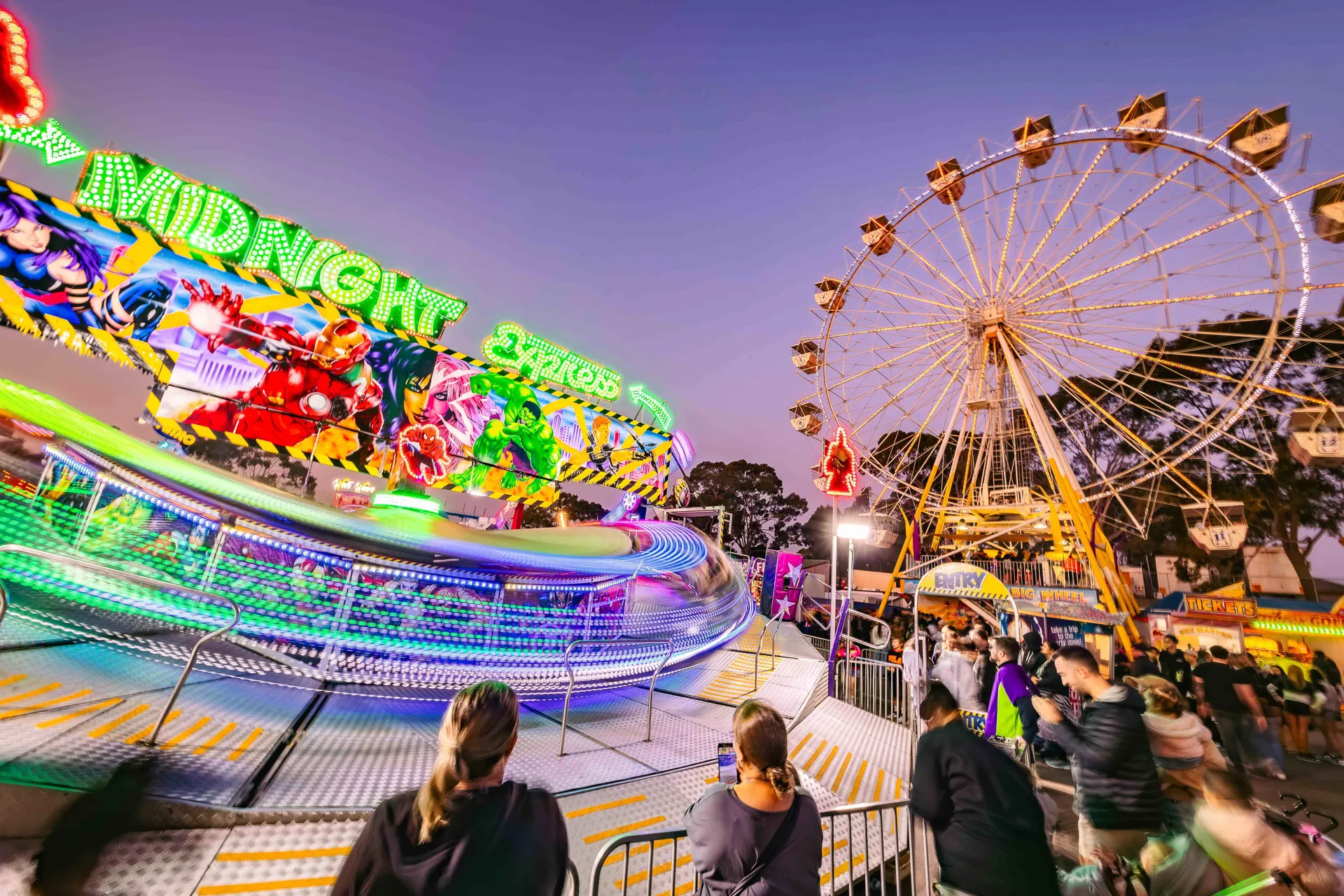 Amusement rides and a Ferris wheel lit up at dusk at the Perth Royal Show carnival.